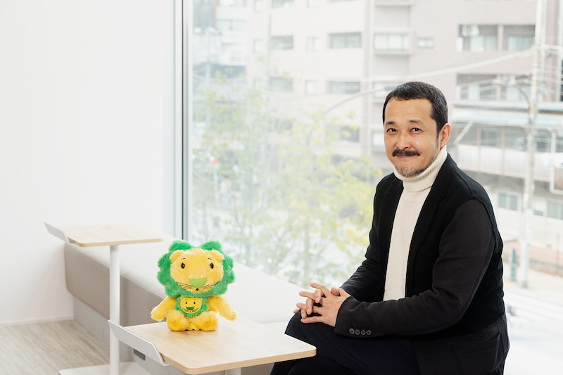 LIONの公式キャラクター、ライオンちゃんのぬいぐるみと一緒に写る、マーケティングデザインセンター部長 大村和顕さんの画像